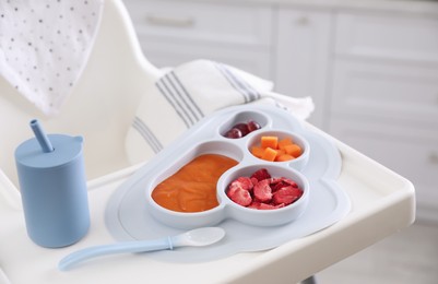 High chair with food in baby tableware on white tray indoors, closeup