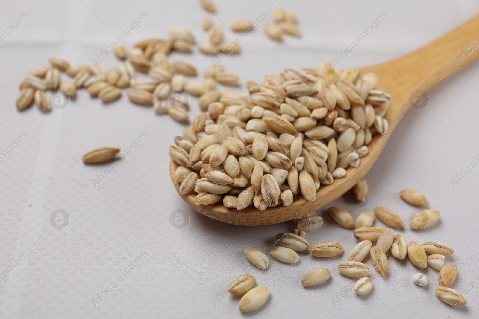 Photo of Wooden spoon with dry pearl barley on white table, closeup