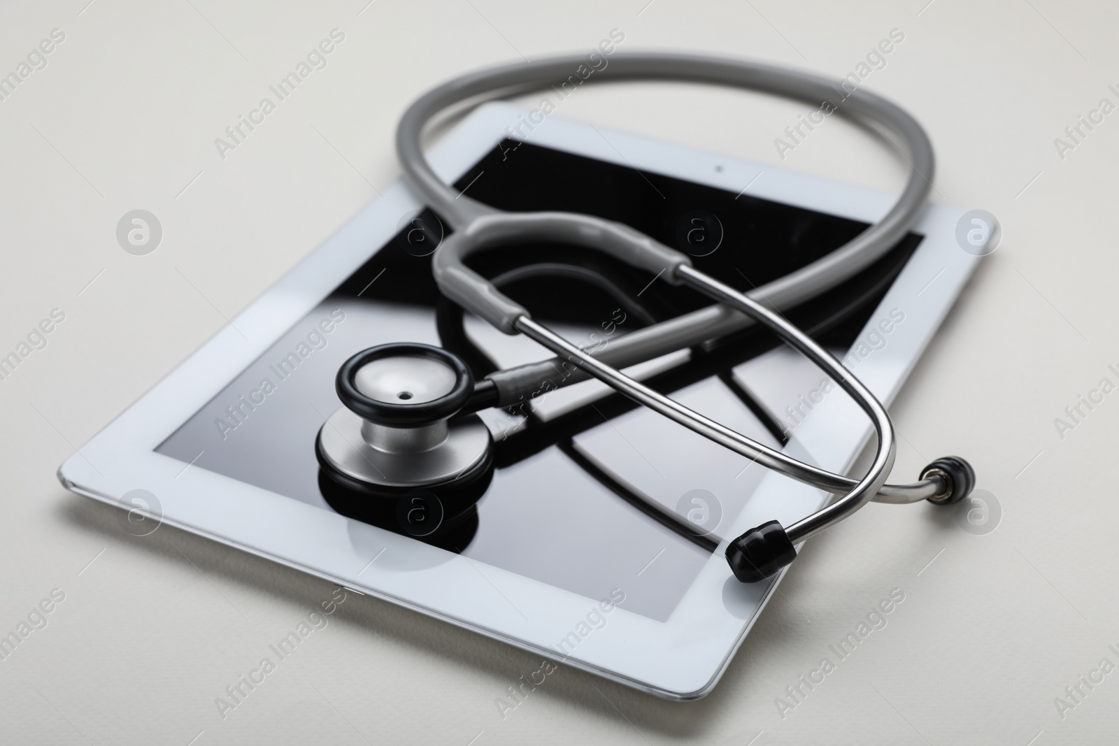 Photo of Medical stethoscope and tablet on beige background, closeup