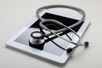 Medical stethoscope and tablet on beige background, closeup