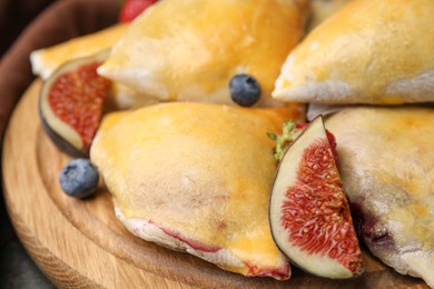 Photo of Delicious samosas with figs and blueberries on wooden board, closeup