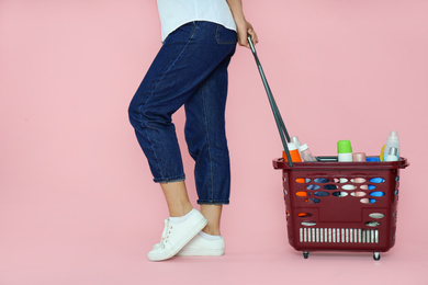 Photo of Woman with shopping basket full of cleaning supplies on pink background, closeup