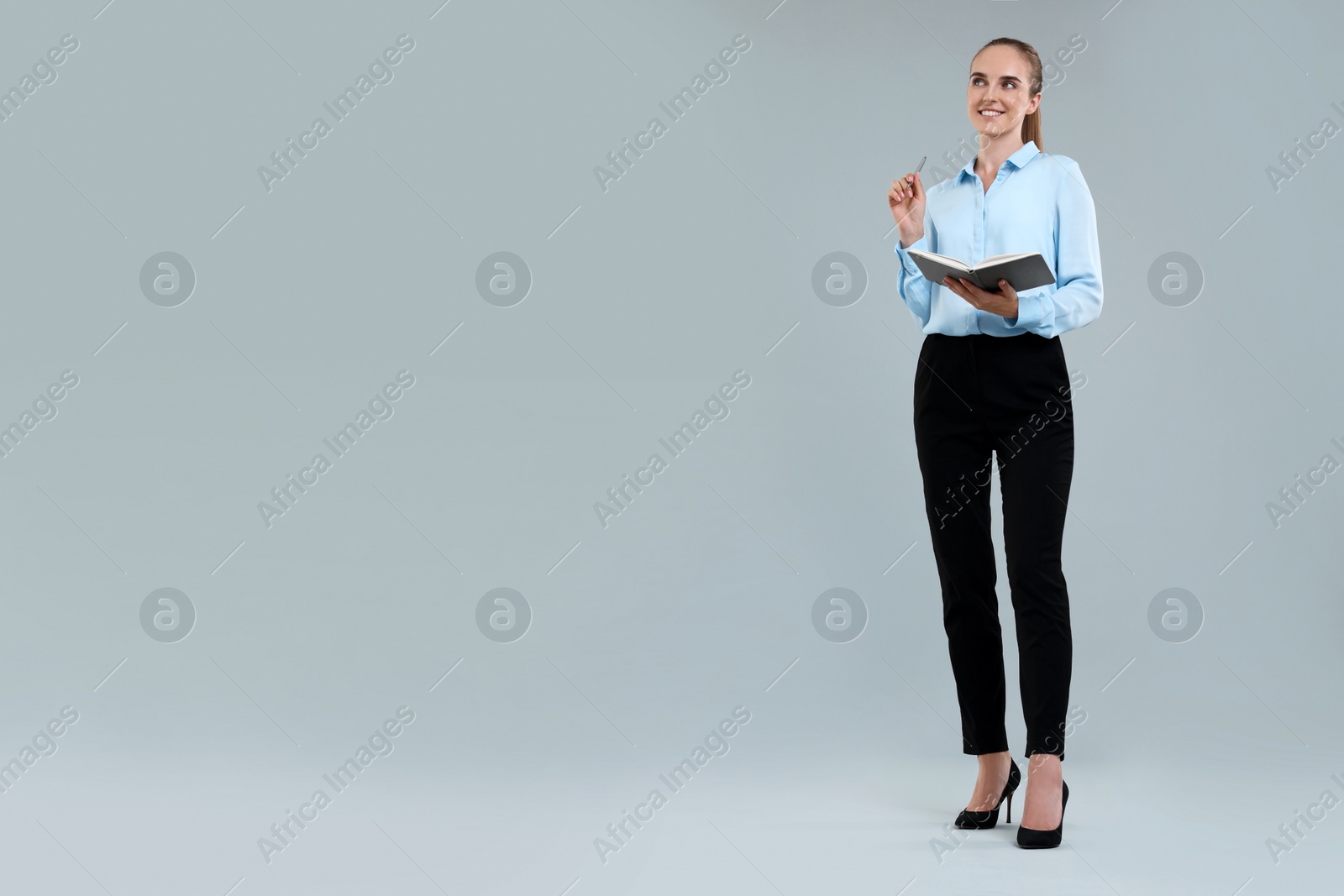 Photo of Happy young secretary with notebook and pen on grey background. Space for text