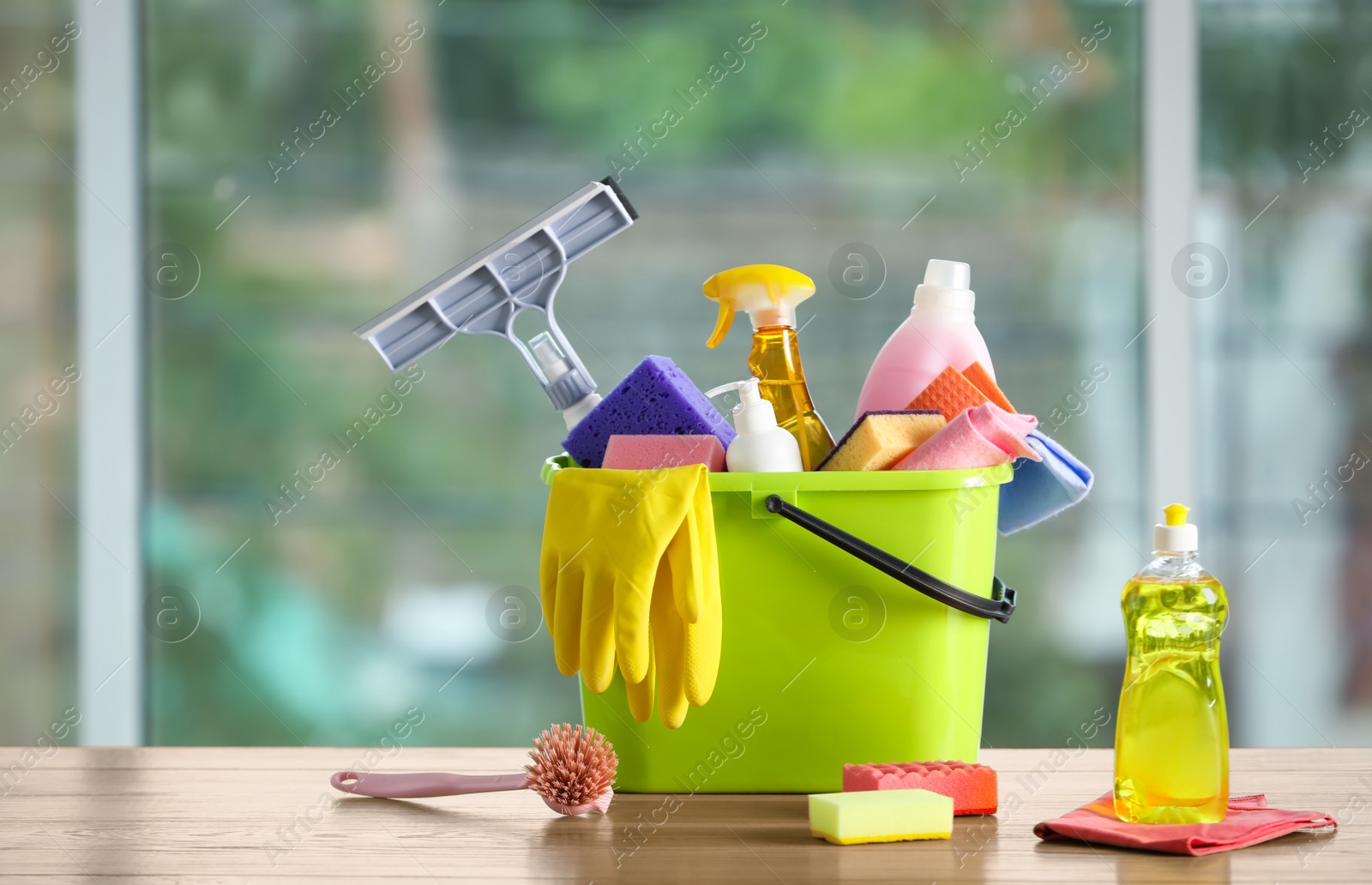 Photo of Light green bucket with cleaning products on wooden table indoors