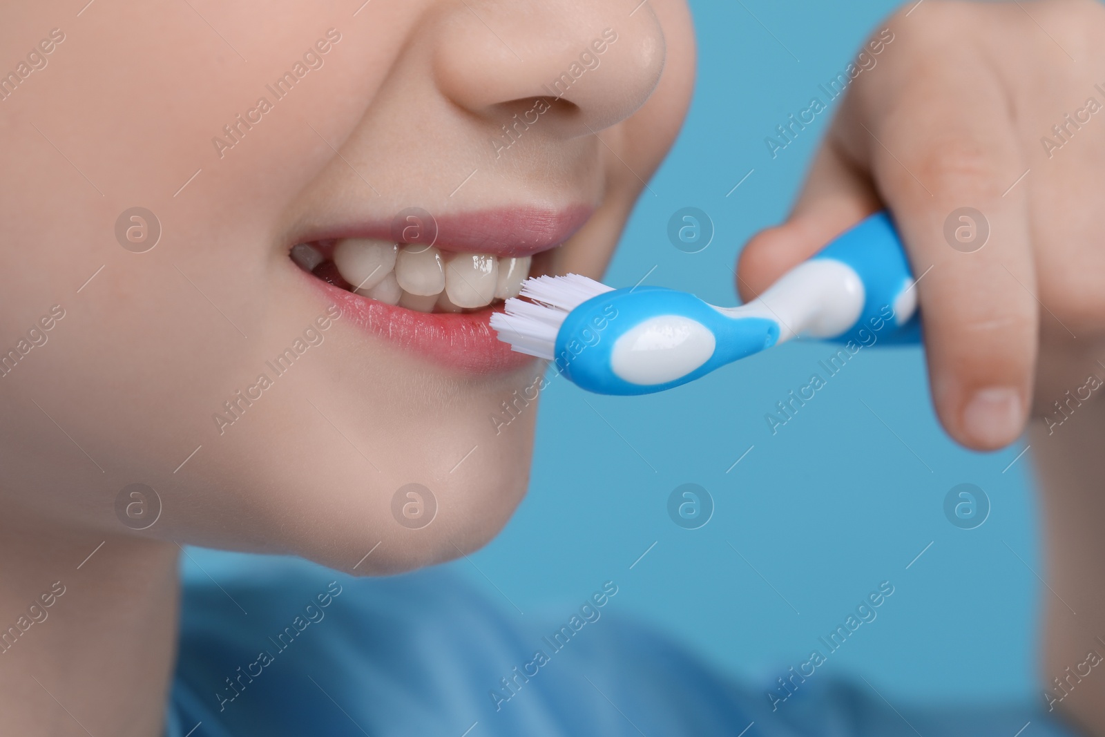 Photo of Girl brushing her teeth with toothbrush on light blue background, closeup