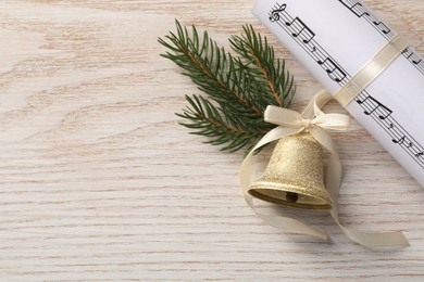 Photo of Golden shiny bell with bow, music sheet and fir twig on wooden table, flat lay. Space for text. Christmas decoration