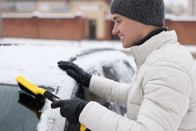 Photo of Man cleaning snow from car windshield outdoors
