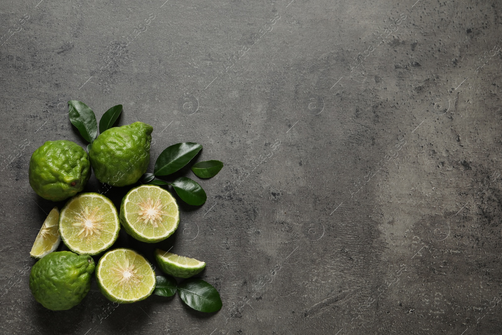 Photo of Fresh ripe bergamot fruits with green leaves on grey table, flat lay. Space for text