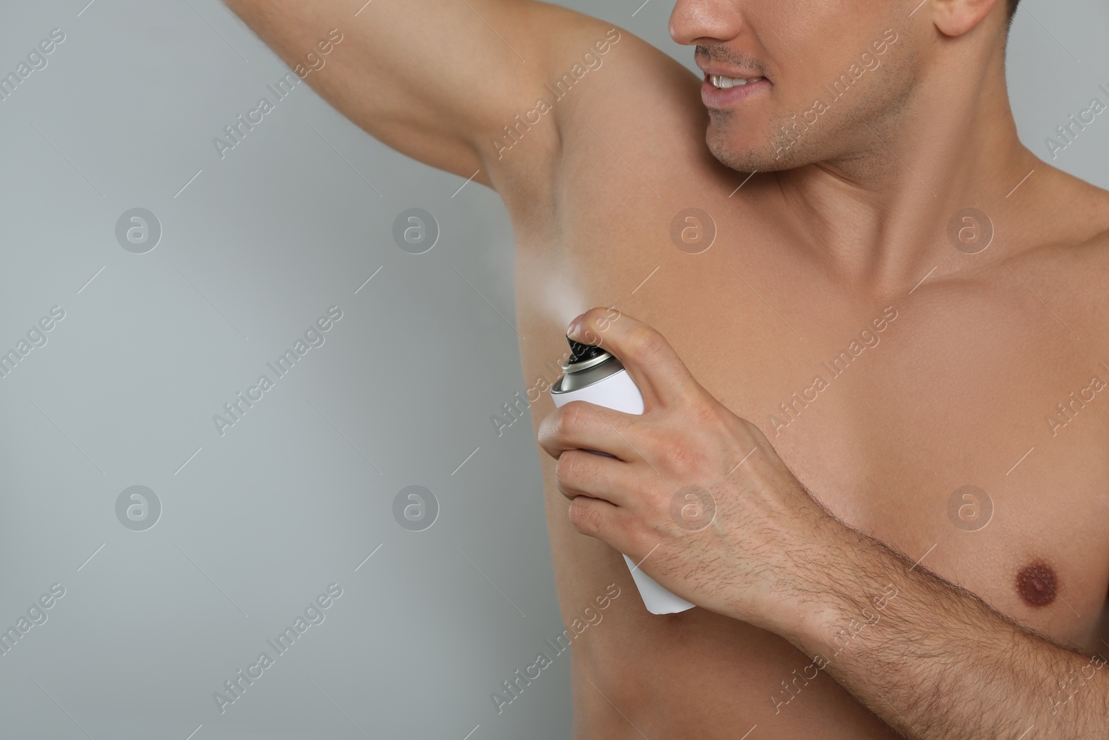 Photo of Man applying deodorant to armpit on grey background, closeup. Space for text