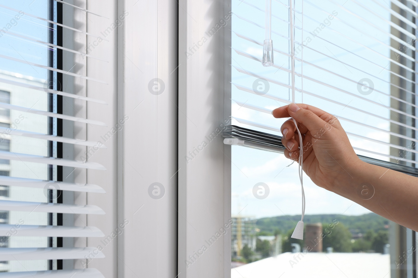 Photo of Woman opening horizontal blinds on window indoors, closeup