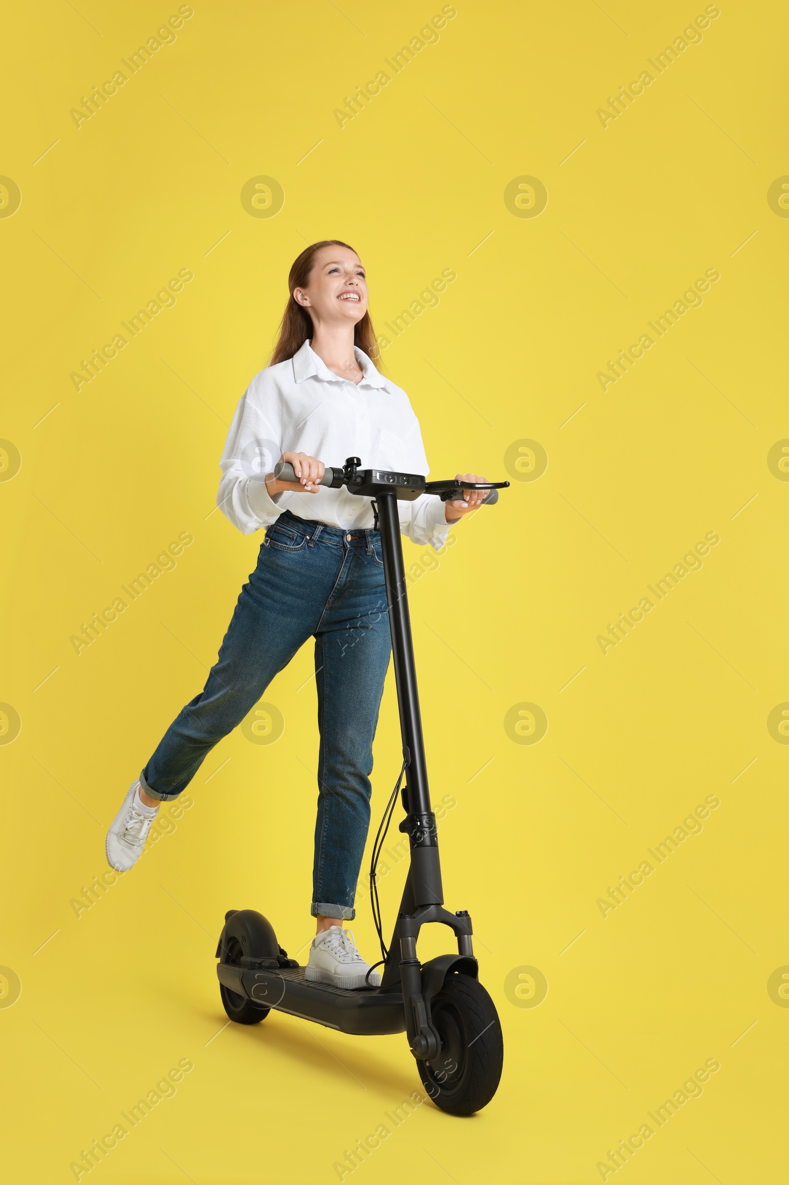 Photo of Happy woman riding modern electric kick scooter on yellow background