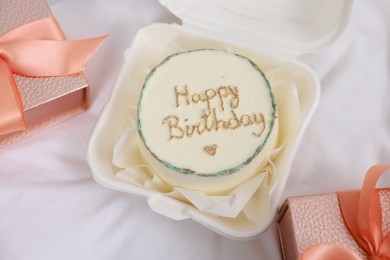 Photo of Delicious decorated cake and gifts on white cloth, flat lay. Happy Birthday