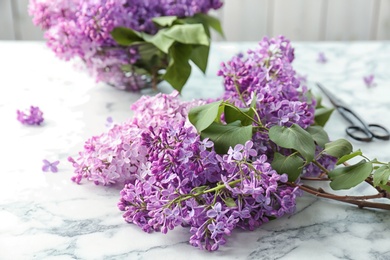 Photo of Beautiful blossoming lilac and scissors on table. Spring flowers