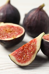 Whole and cut ripe figs on white wooden table, closeup