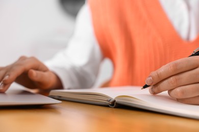 Young woman writing in notebook while working on laptop at wooden table, closeup