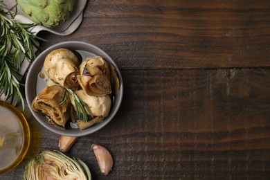 Bowl with delicious artichokes pickled in olive oil and ingredients on wooden table, flat lay. Space for text