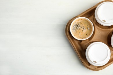 Photo of Takeaway paper coffee cups in cardboard holder on white wooden table, top view. Space for text