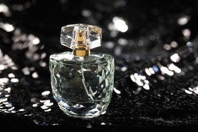 Photo of Luxury perfume in bottle on fabric with shiny sequins, closeup