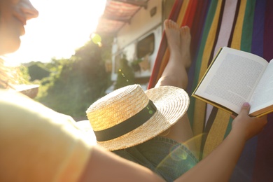 Photo of Young woman reading book in hammock near motorhome outdoors on sunny day, closeup