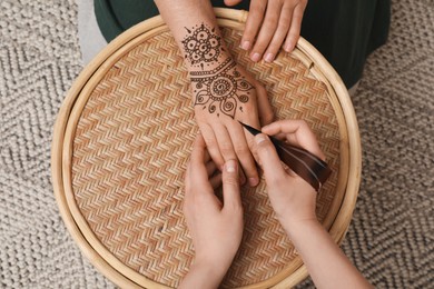 Photo of Master making henna tattoo on hand at table, top view. Traditional mehndi