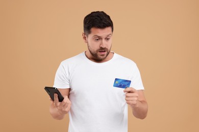 Photo of Emotional man with credit card and smartphone on beige background. Be careful - fraud