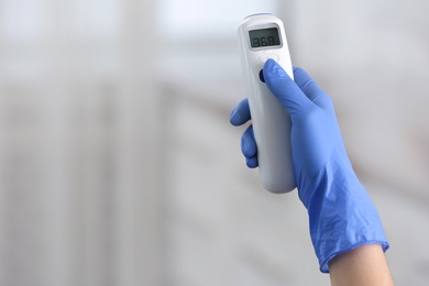 Photo of Closeup view of doctor with infrared thermometer on blurred background, space for text. Checking temperature during Covid-19 pandemic