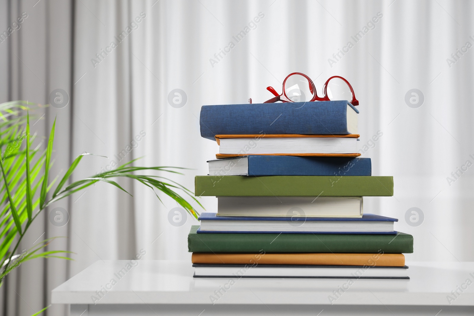 Photo of Hardcover books and glasses on white chest of drawers indoors