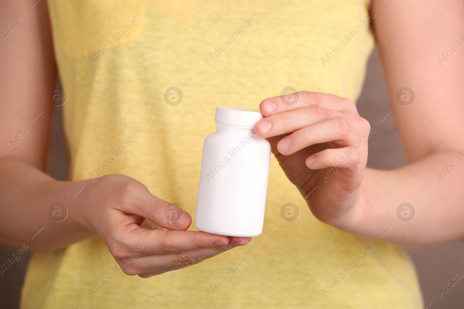 Photo of Woman holding blank white bottle with vitamin pills against light brown background, closeup