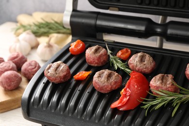 Photo of Electric grill with vegetables, meat balls and rosemary on table, closeup