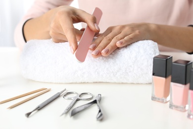 Photo of Woman filing nails covered with polish at table, closeup