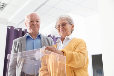 Photo of Elderly woman putting ballot paper into box at polling station