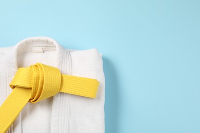 Photo of Yellow karate belt and kimono on light blue background, top view. Space for text