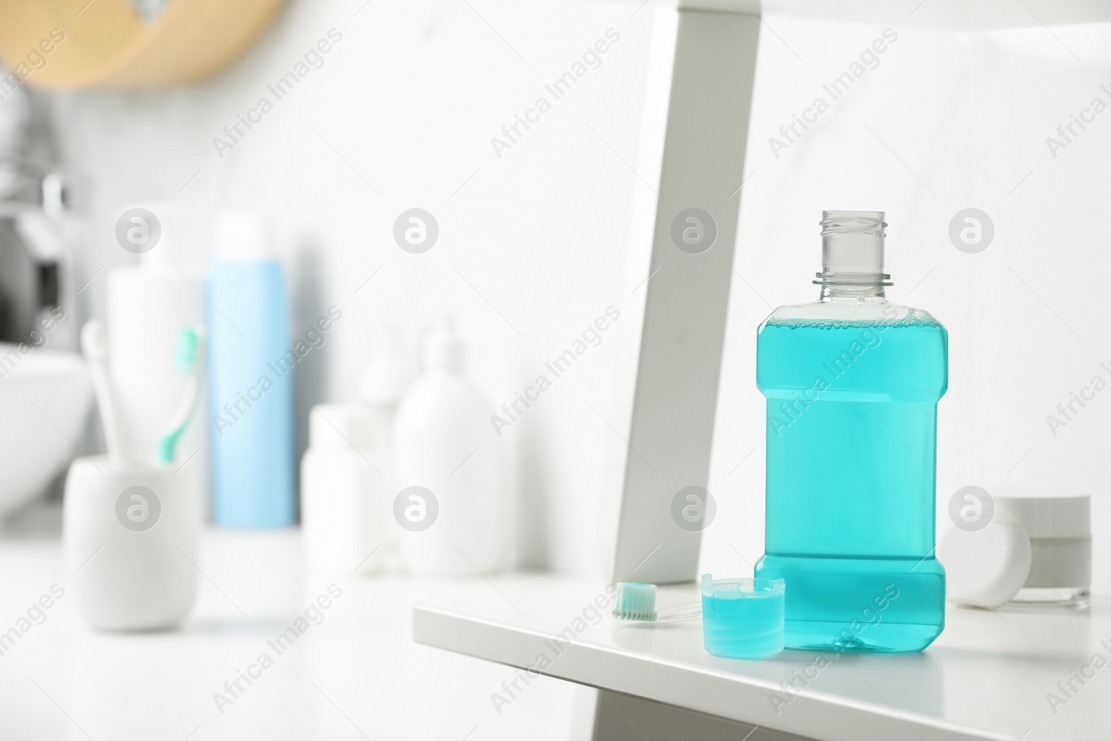 Photo of Bottle of mouthwash on white shelf in bathroom, space for text