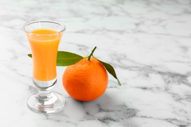 Photo of Delicious tangerine liqueur in shot glass and fresh fruit on white marble table, closeup. Space for text