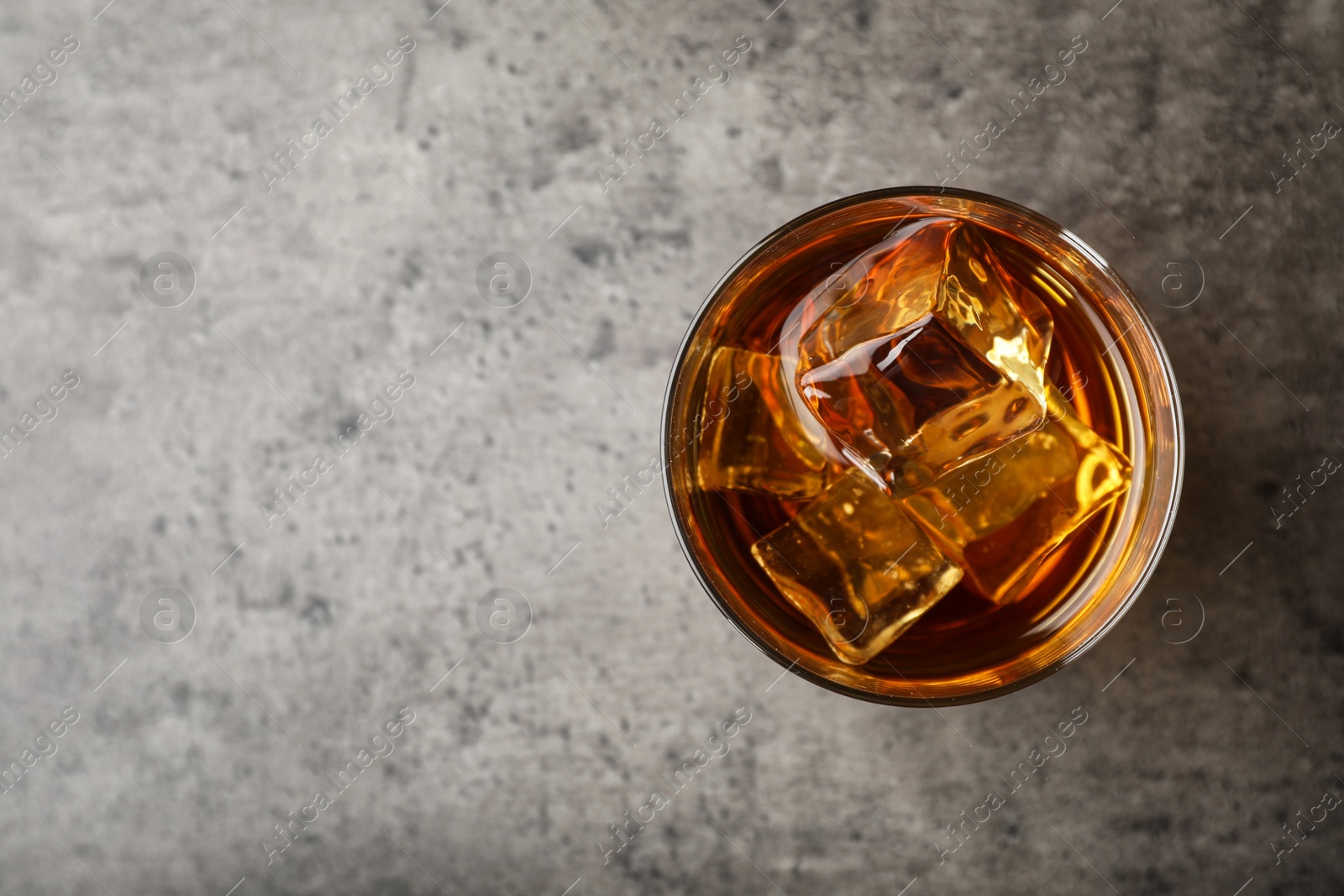 Photo of Golden whiskey in glass with ice cubes on table, top view. Space for text