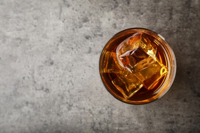 Photo of Golden whiskey in glass with ice cubes on table, top view. Space for text