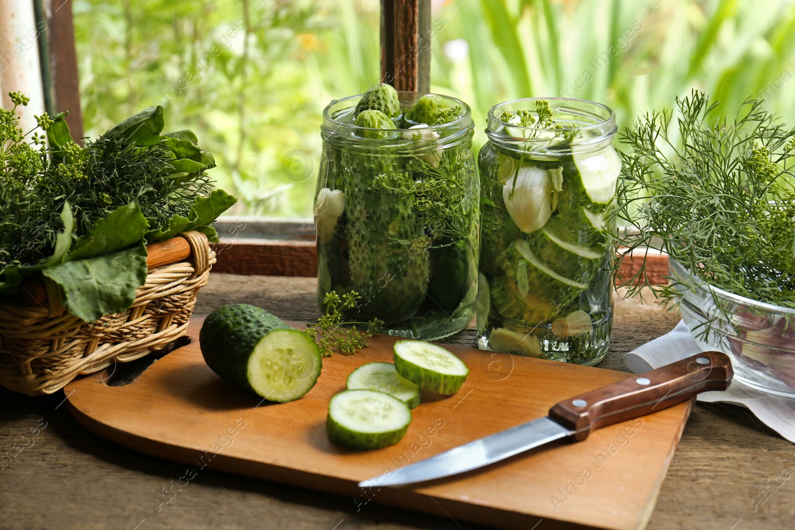 Photo of Glass jars, fresh cucumbers and herbs on wooden table indoors. Pickling recipe