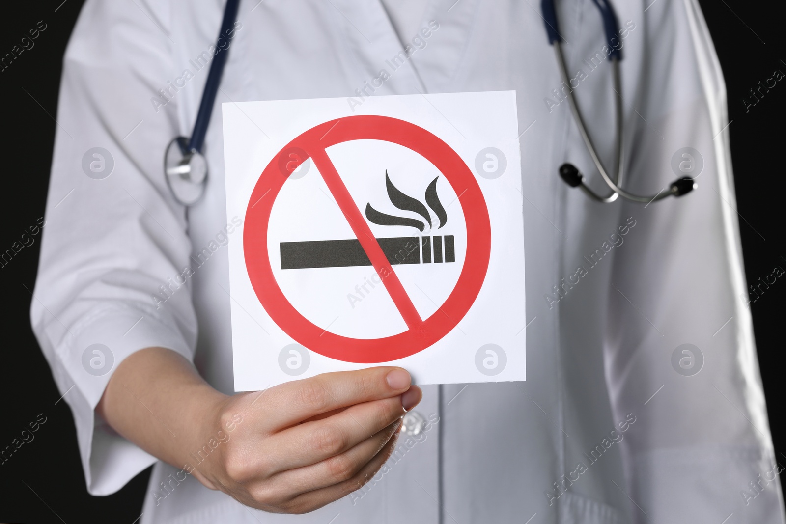 Photo of Doctor holding card with no smoking sign on black background, closeup