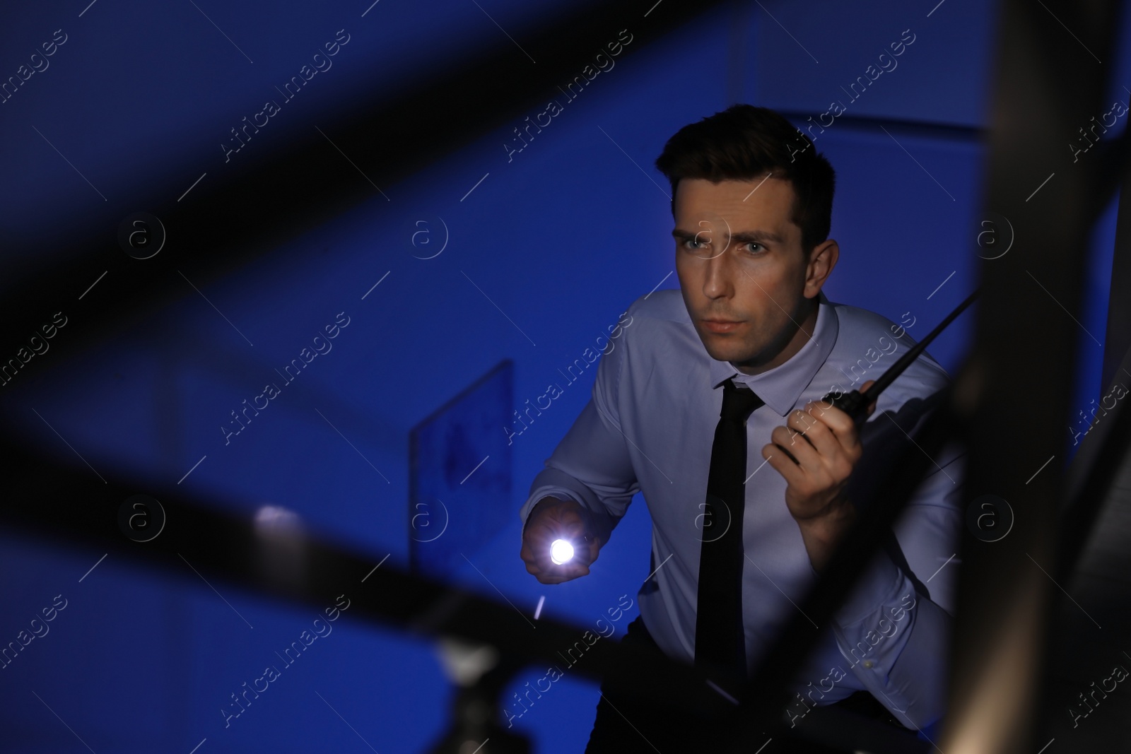 Photo of Male security guard with flashlight and portable radio transmitter in dark room