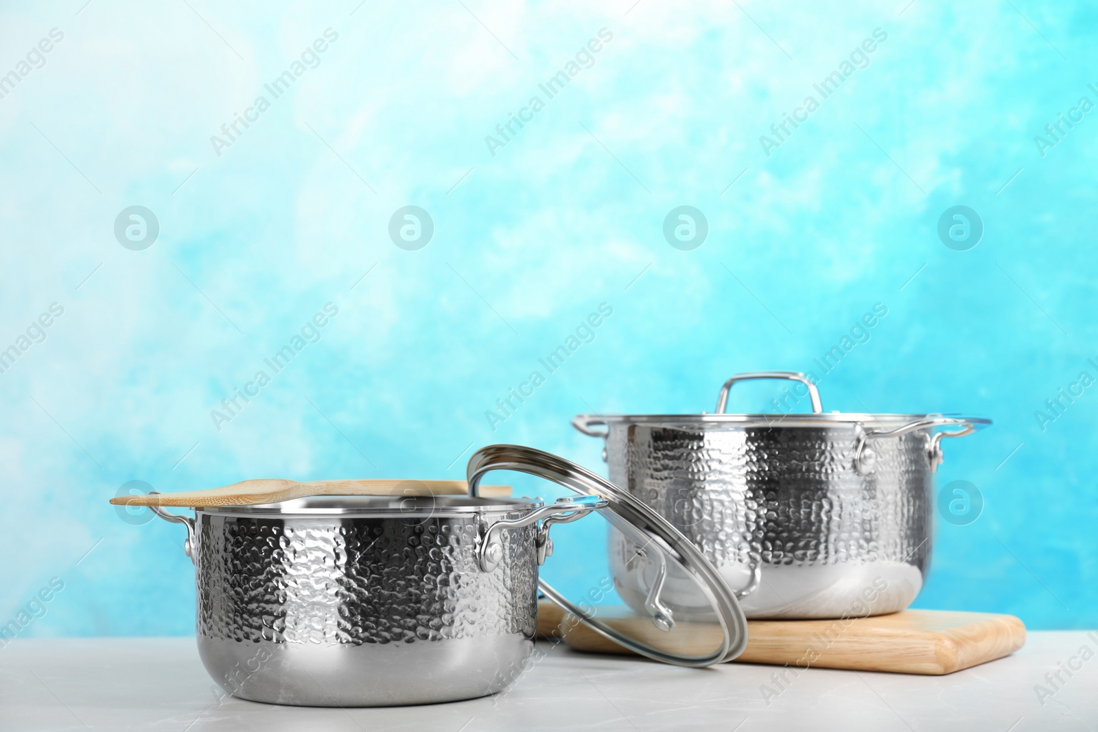 Photo of New clean saucepans on table against color background, space for text