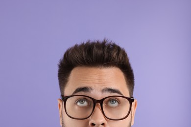 Photo of Man in glasses looking up on violet background, closeup