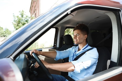 Photo of Young courier with parcels in delivery car