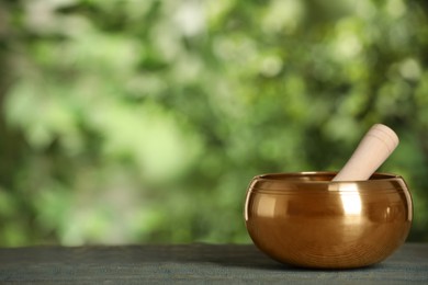 Golden singing bowl with mallet on blue wooden table outdoors, space for text