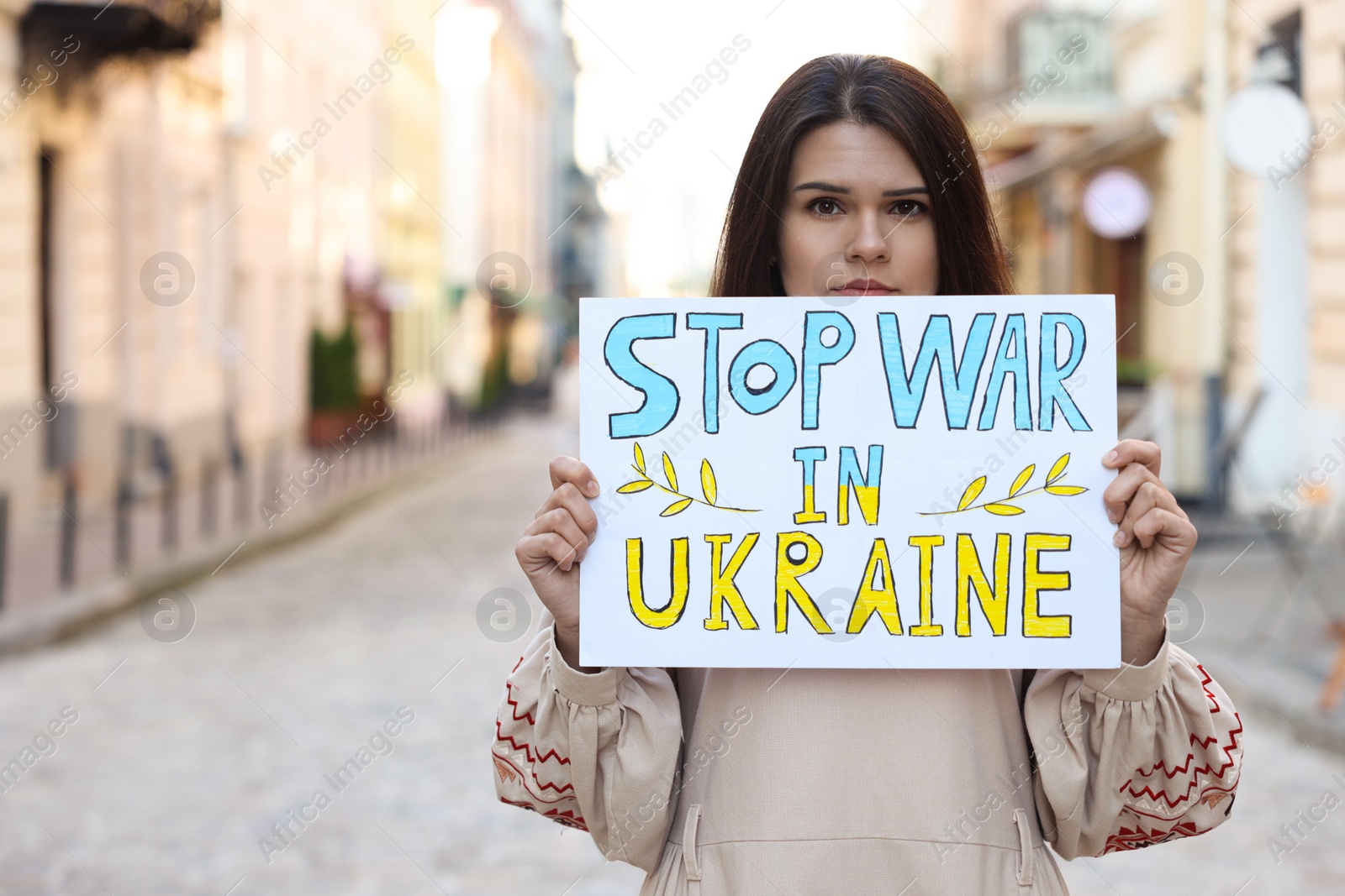 Photo of Sad woman holding poster Stop War in Ukraine on city street. Space for text