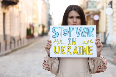 Photo of Sad woman holding poster Stop War in Ukraine on city street. Space for text