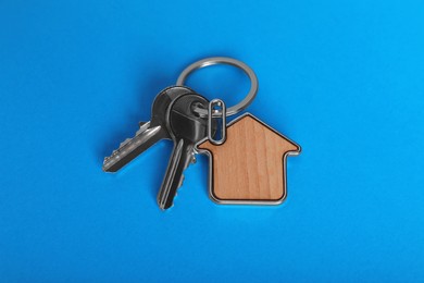 Keys with trinket in shape of house on blue background, above view. Real estate agent services