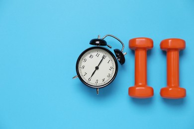 Alarm clock and dumbbells on light blue background, flat lay with space for text. Morning exercise