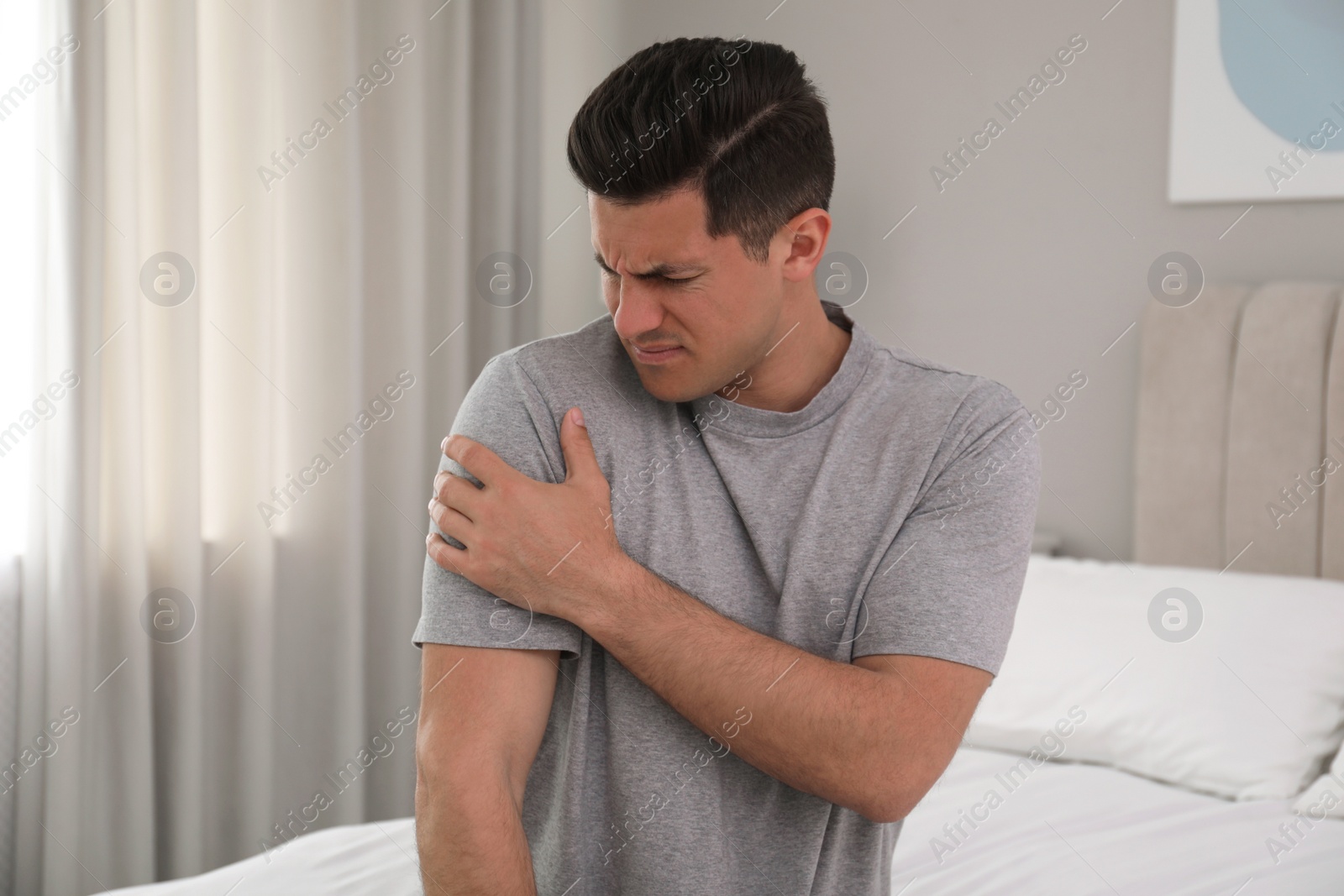 Photo of Man suffering from shoulder pain on bed at home