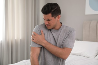 Photo of Man suffering from shoulder pain on bed at home