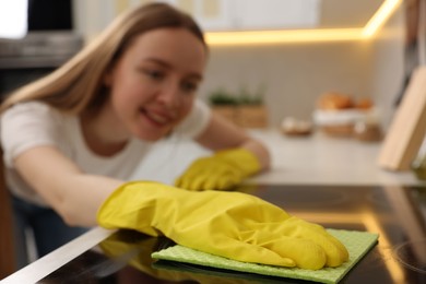 Photo of Woman with spray bottle and microfiber cloth cleaning electric stove in kitchen, selective focus